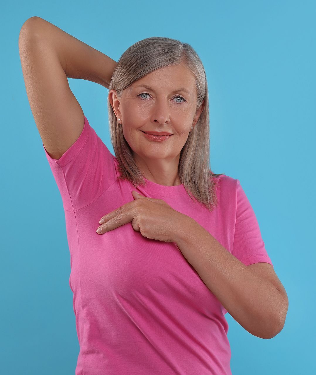 Beautiful senior woman doing breast self-examination on light blue background, space for text